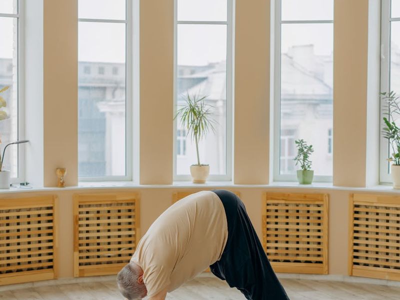 Man stretching on a yoga mat in a spacious, well-lit room.